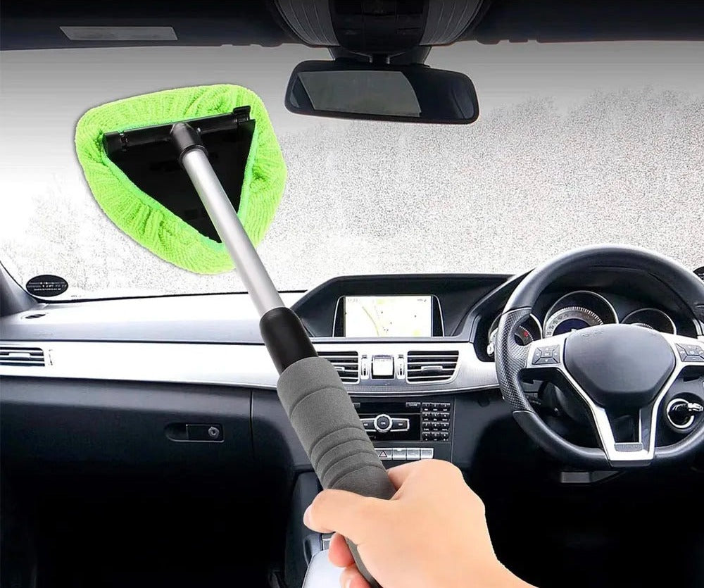 Telescopic windscreen cleaning tool with green microfibre pad being used inside a car on a misted windscreen
